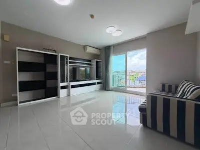 Spacious living room with modern entertainment unit and striped sofa, featuring large windows and balcony access.