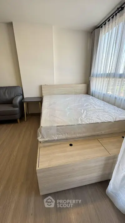 Modern bedroom with wooden flooring, cozy bed, and natural light from large window.