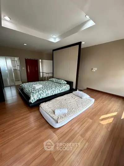 Spacious bedroom with wooden flooring and modern design, featuring a double bed and a single mattress.