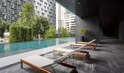 Luxurious condominium pool area with modern lounge chairs and lush greenery.