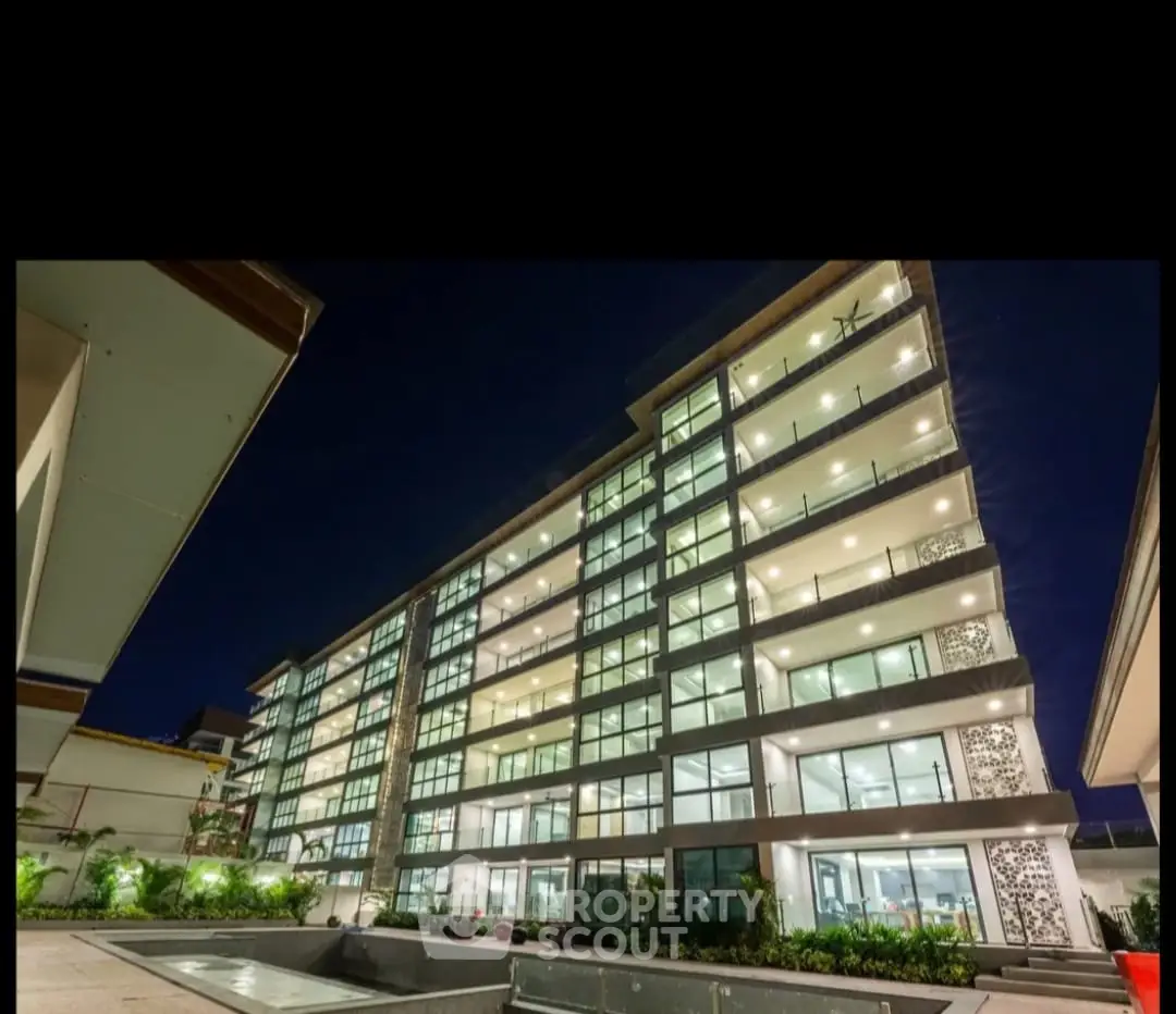 Modern multi-story residential building with illuminated balconies and landscaped surroundings at night.
