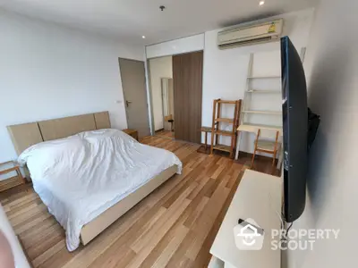 Modern bedroom with wooden flooring, wall-mounted TV, and air conditioning in a stylish apartment.