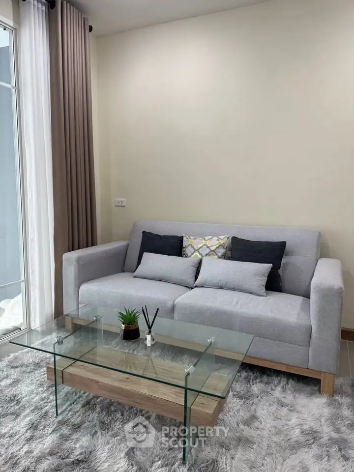 Modern living room with stylish gray sofa and glass coffee table on plush rug.