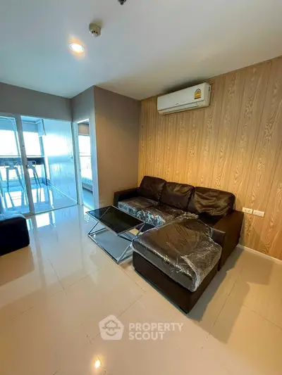 Modern living room with sleek black sofa and glass coffee table, featuring a stylish wood accent wall and air conditioning.