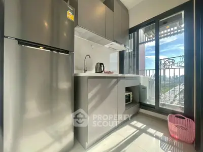 Modern kitchen with sleek cabinets and balcony view, featuring stainless steel fridge and kettle.