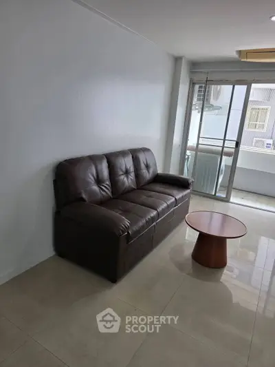 Modern living room with leather sofa and small round table near balcony.