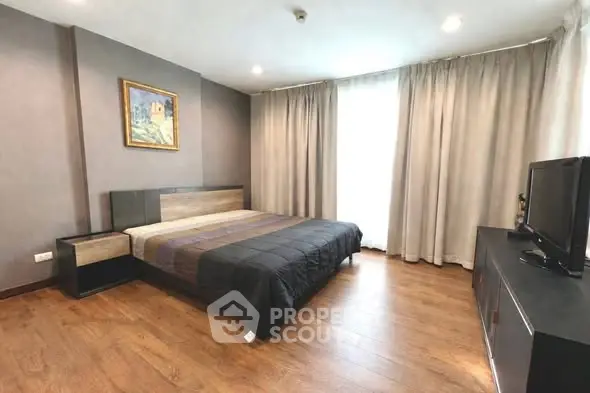 Spacious modern bedroom with wooden flooring and large window for natural light.