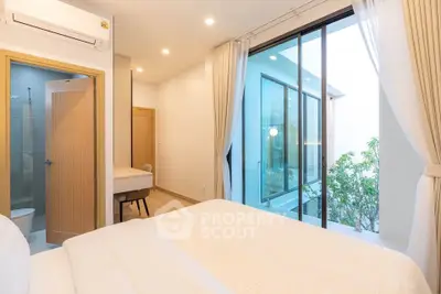 Modern bedroom with large windows and ensuite bathroom, featuring minimalist decor and natural light.