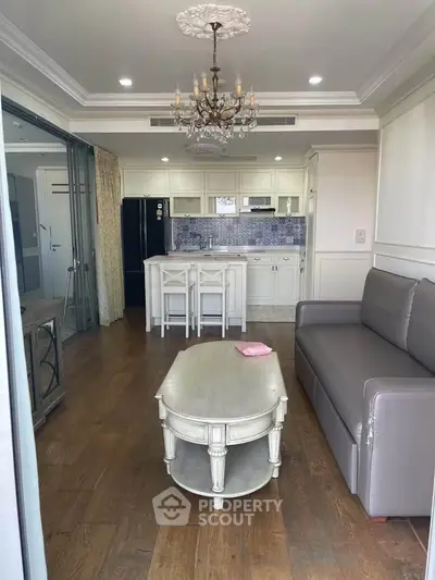Charming living room with elegant chandelier and open kitchen layout, featuring modern appliances and stylish decor.