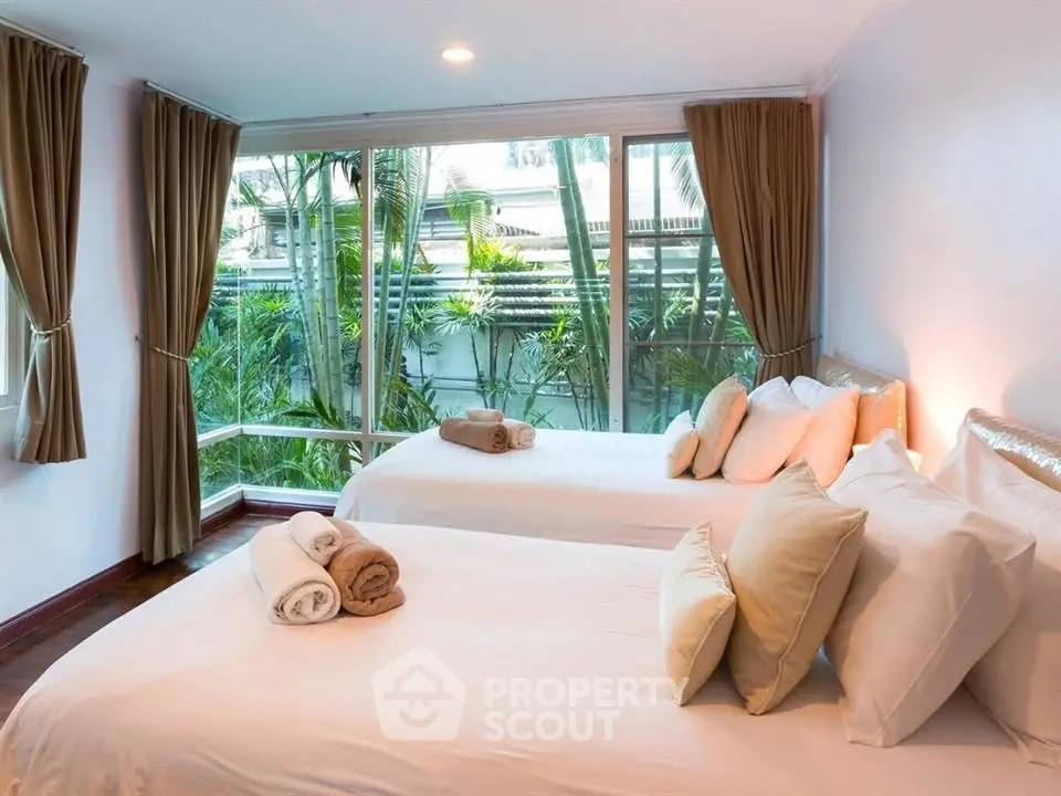 Spacious bedroom with large windows and garden view, featuring two neatly made beds and elegant decor.