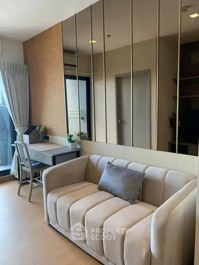 Modern living room with elegant sofa and mirrored wall, featuring a cozy workspace by the window.