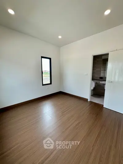 Spacious empty room with wooden flooring and attached bathroom, ideal for customization.