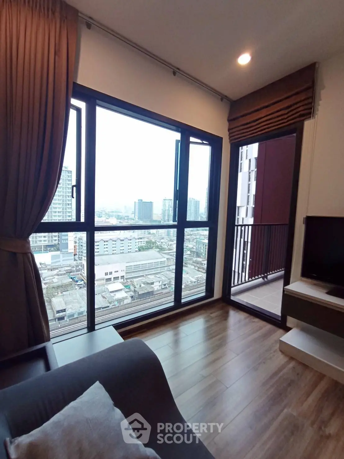 Modern living room with large window offering stunning city view and access to a cozy balcony.