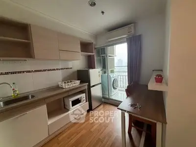 Modern kitchen with balcony view, featuring wooden cabinets, fridge, and microwave in a cozy apartment.