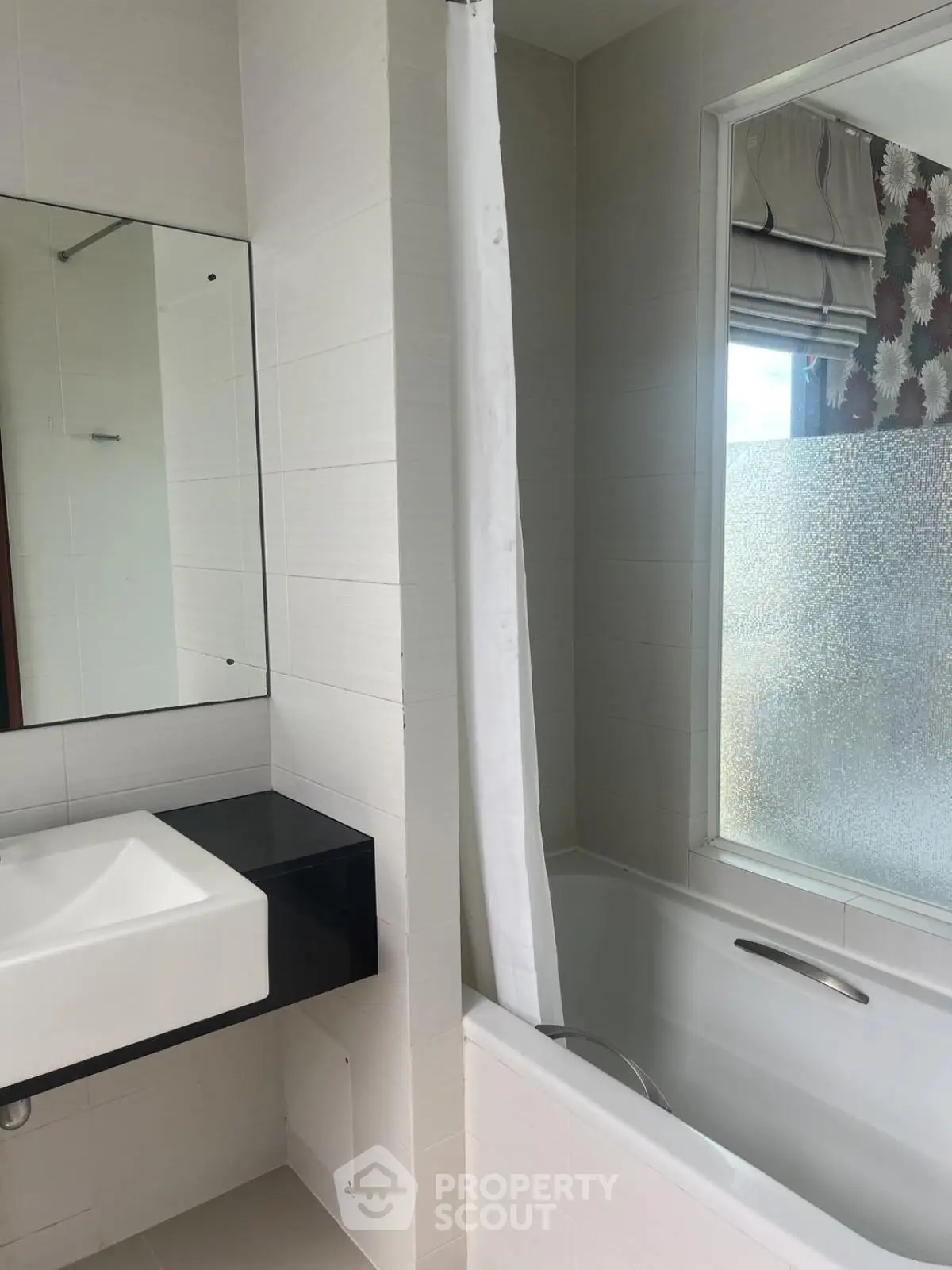 Modern bathroom with sleek sink and bathtub, featuring frosted glass window for privacy.