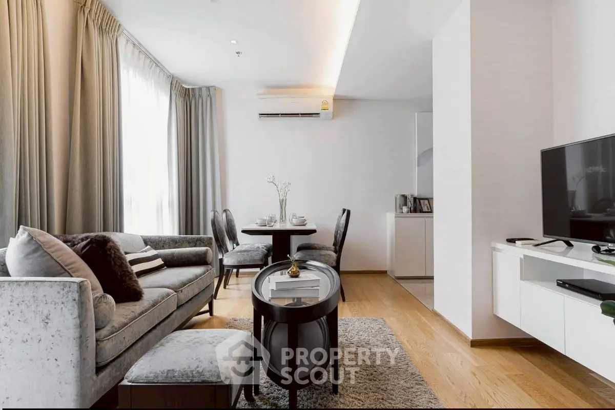 Elegant living room with modern decor, plush sofa, dining area, and sleek TV setup in a bright apartment.