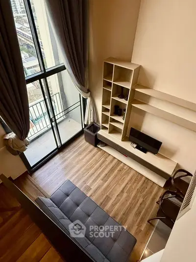 Modern loft-style living room with high ceilings and large windows offering city views.
