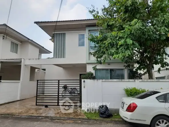 Modern two-story house with gated driveway and lush greenery