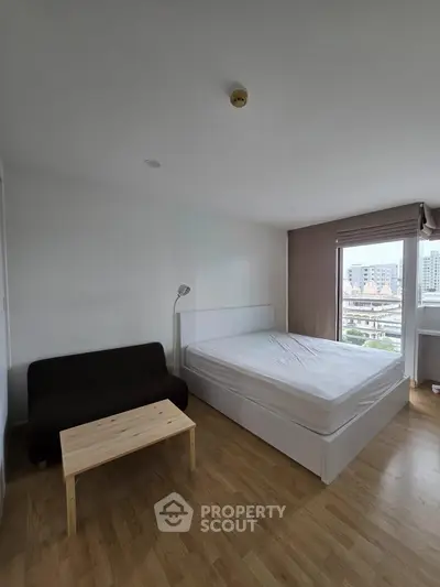 Modern bedroom with city view, featuring a cozy bed, sofa, and wooden flooring for a comfortable living space.
