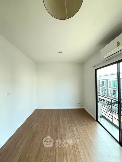 Spacious empty room with wooden flooring and balcony access in modern apartment.