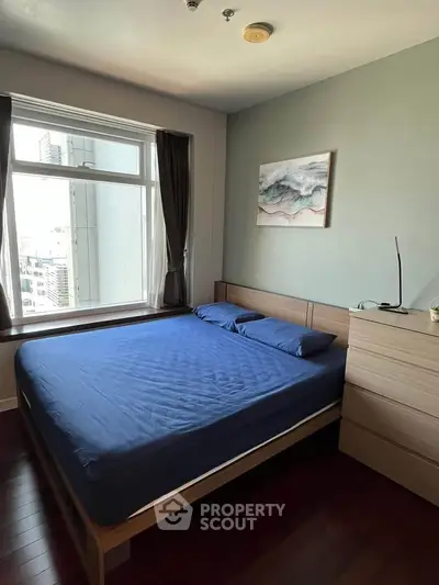 Modern bedroom with large window and city view, featuring a stylish bed and wooden furniture.