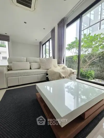 Modern living room with large windows and stylish furniture, offering a serene garden view.