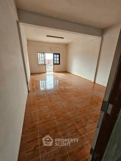 Spacious empty room with glossy wooden flooring and large windows for natural light.