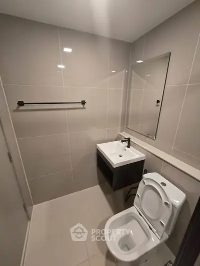 Modern bathroom with sleek fixtures and neutral tiles, featuring a compact sink and toilet.