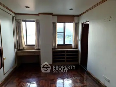 Spacious room with wooden flooring and large windows offering natural light