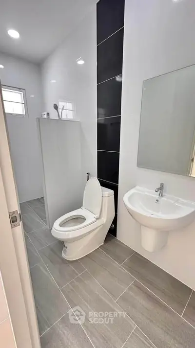 Modern bathroom with sleek design, featuring a toilet, sink, and shower area with elegant tile flooring.