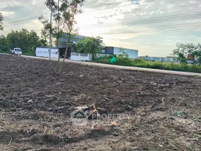 Expansive plot of land with potential for development, surrounded by greenery and a nearby building.