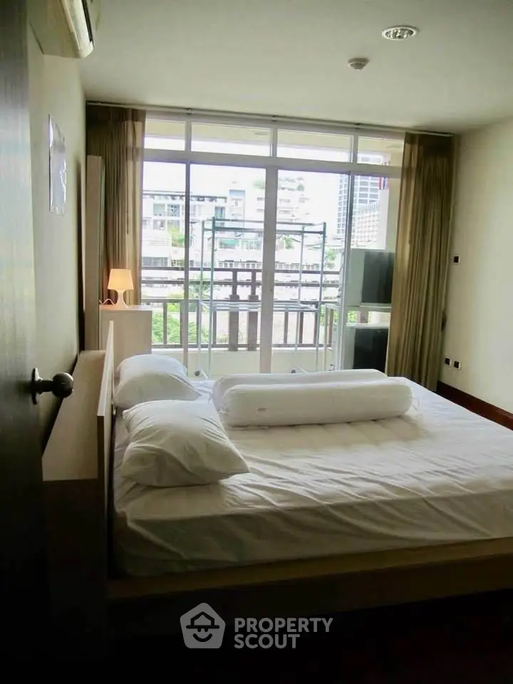 Spacious bedroom with large windows and city view, featuring modern furnishings and natural light.