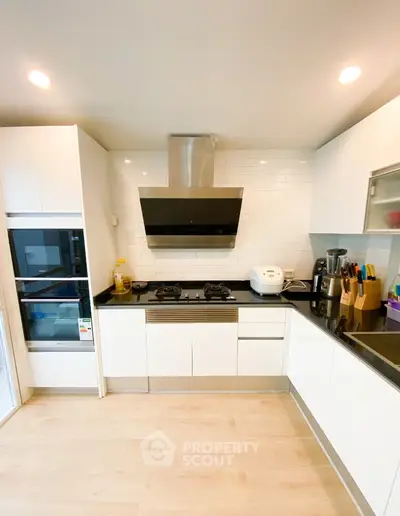 Modern kitchen with sleek white cabinets and black countertops featuring gas stove and built-in oven.