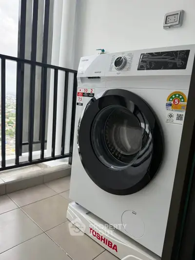 Modern washing machine on a high-rise balcony with city view.