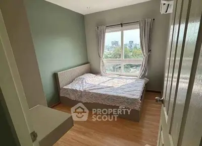 Cozy bedroom with large window offering city views, featuring wooden flooring and modern decor.