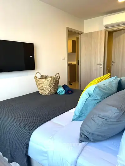 Modern bedroom with stylish decor and wall-mounted TV, featuring cozy bedding and a basket for storage.