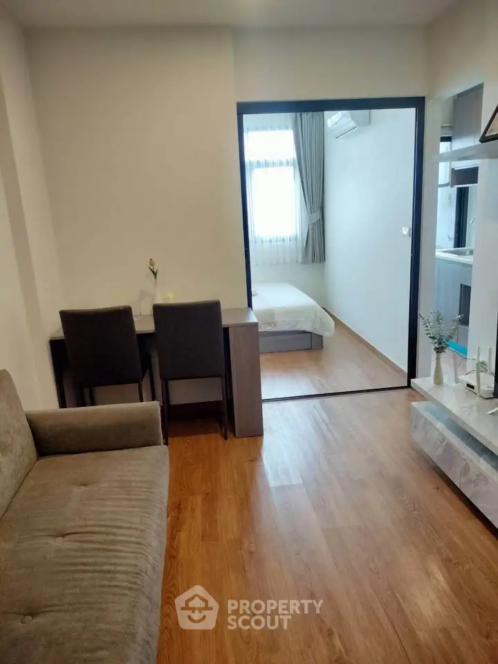 Modern apartment interior with cozy living room and view into a bright bedroom, featuring stylish wooden flooring.