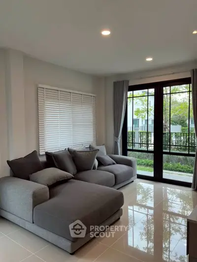 Spacious living room with modern gray sofas and large windows overlooking a lush garden.