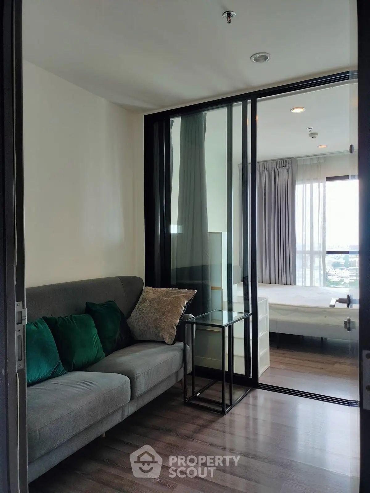 Modern apartment with glass partition, cozy living area, and bright bedroom view.