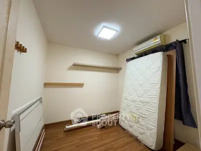 Compact bedroom with wooden flooring and wall-mounted shelves, featuring an air conditioner and a mattress.