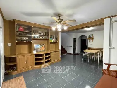 Spacious living room with wooden built-in shelves and dining area, featuring tiled flooring and ceiling fan.