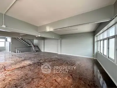 Spacious open-plan interior with large windows and staircase, ideal for versatile use.