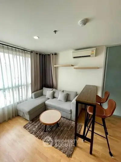 Modern living room with cozy gray sofa, stylish bar stools, and natural light from large window.