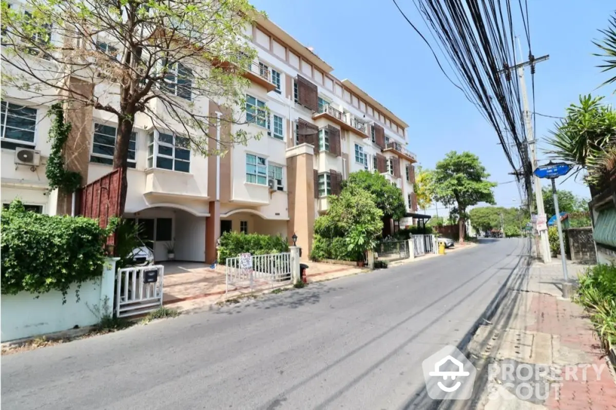 Charming townhouse exterior on a sunny street with lush greenery and modern design.