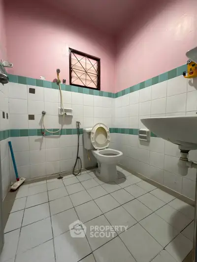 Compact bathroom with pink walls and tiled floor, featuring a toilet and shower area.