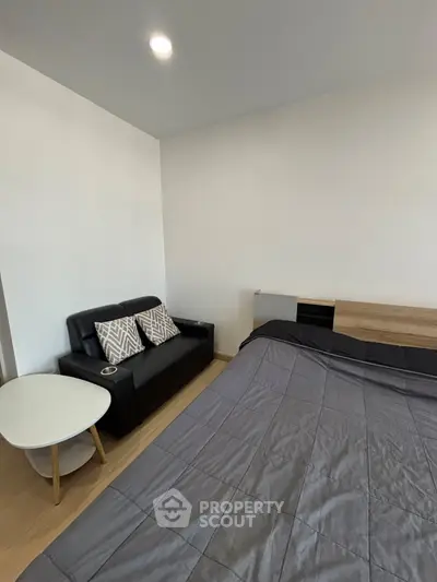 Modern bedroom with sleek black sofa and cozy bed, perfect for urban living.