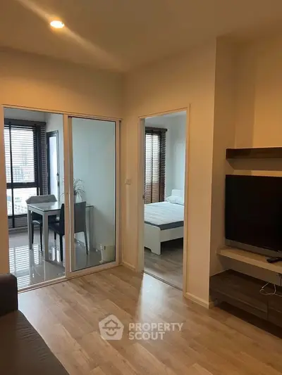 Modern apartment interior with open living space and bedroom, featuring sleek wooden flooring and natural light.