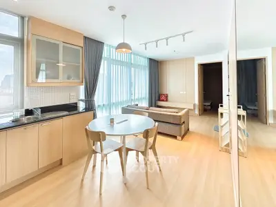 Modern open-layout living room with kitchen, featuring sleek furniture and large windows.