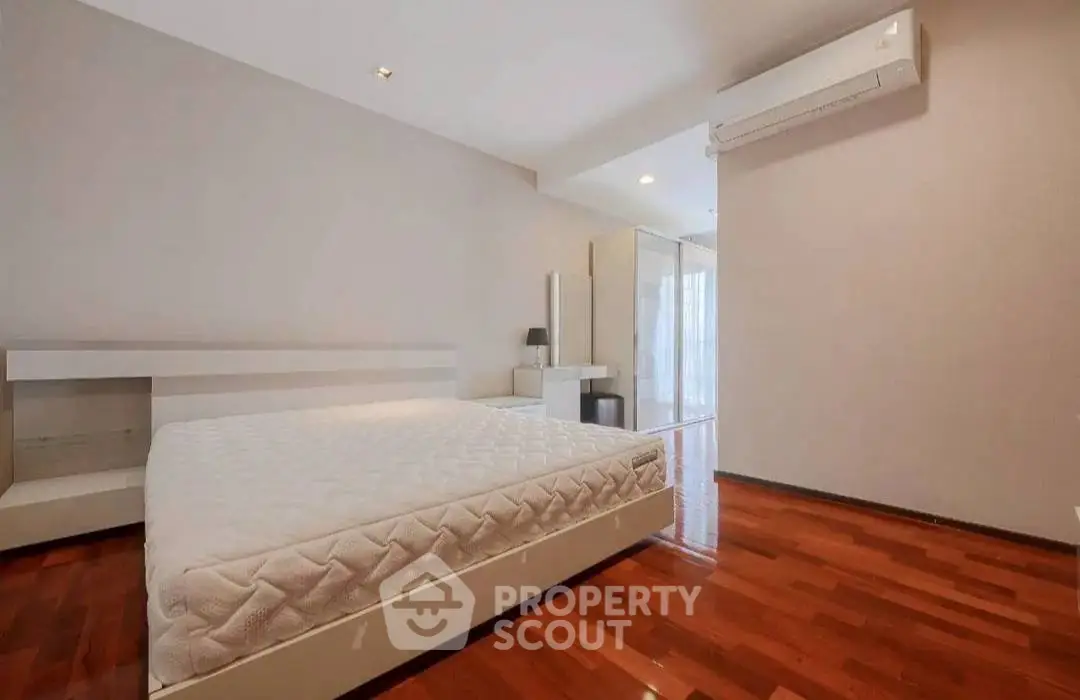 Spacious bedroom with wooden flooring and modern air conditioning unit.