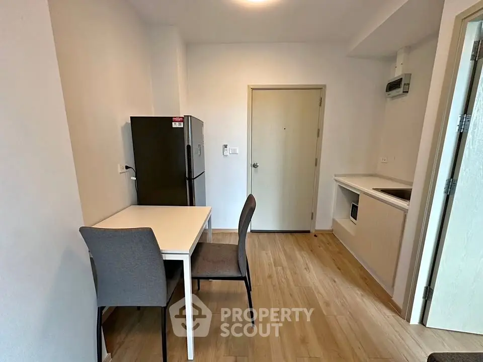 Modern apartment interior with dining area and kitchenette, featuring sleek furniture and wooden flooring.